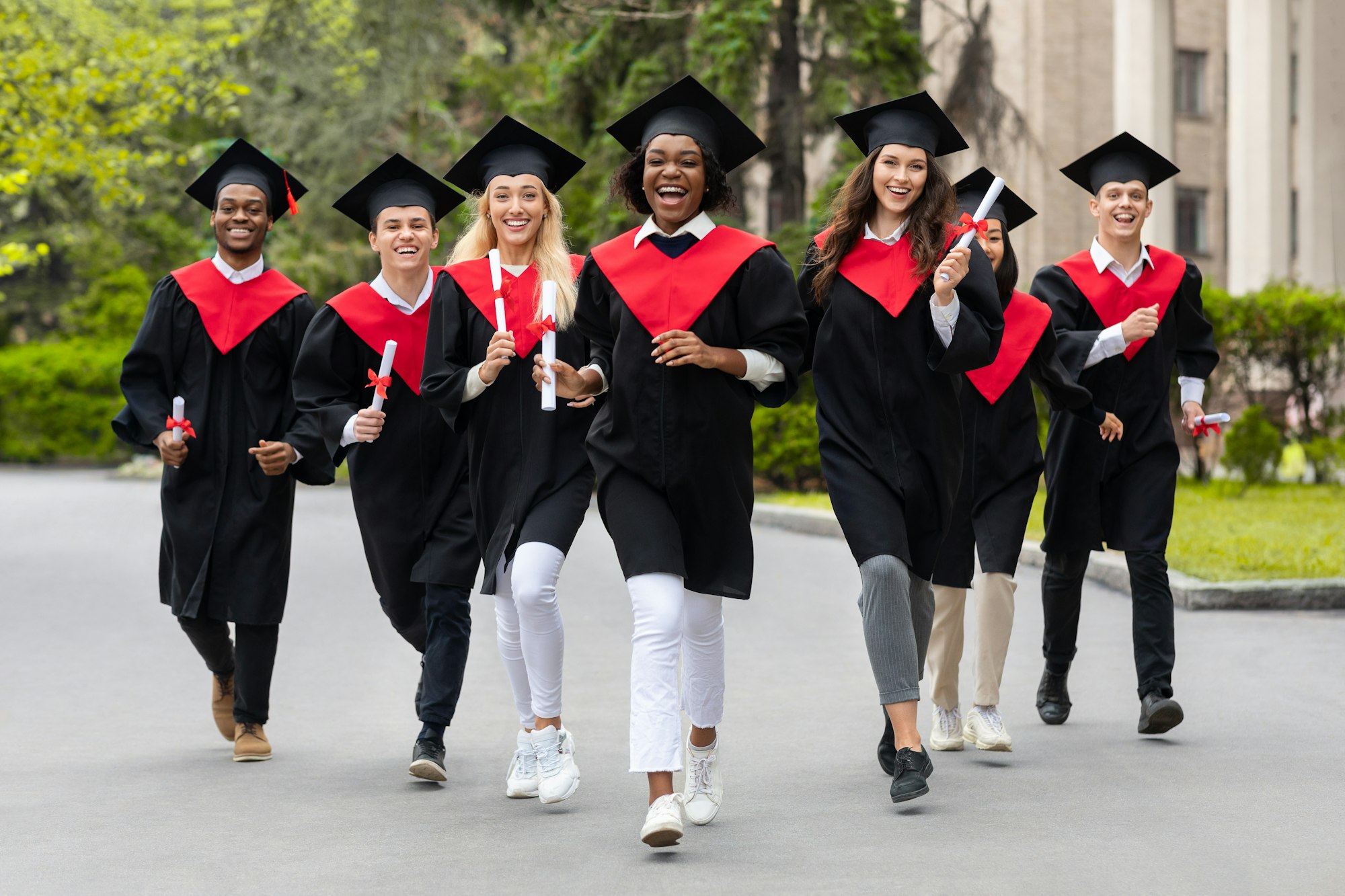 Cheerful multiracial students in graduation costumes walking by university campus